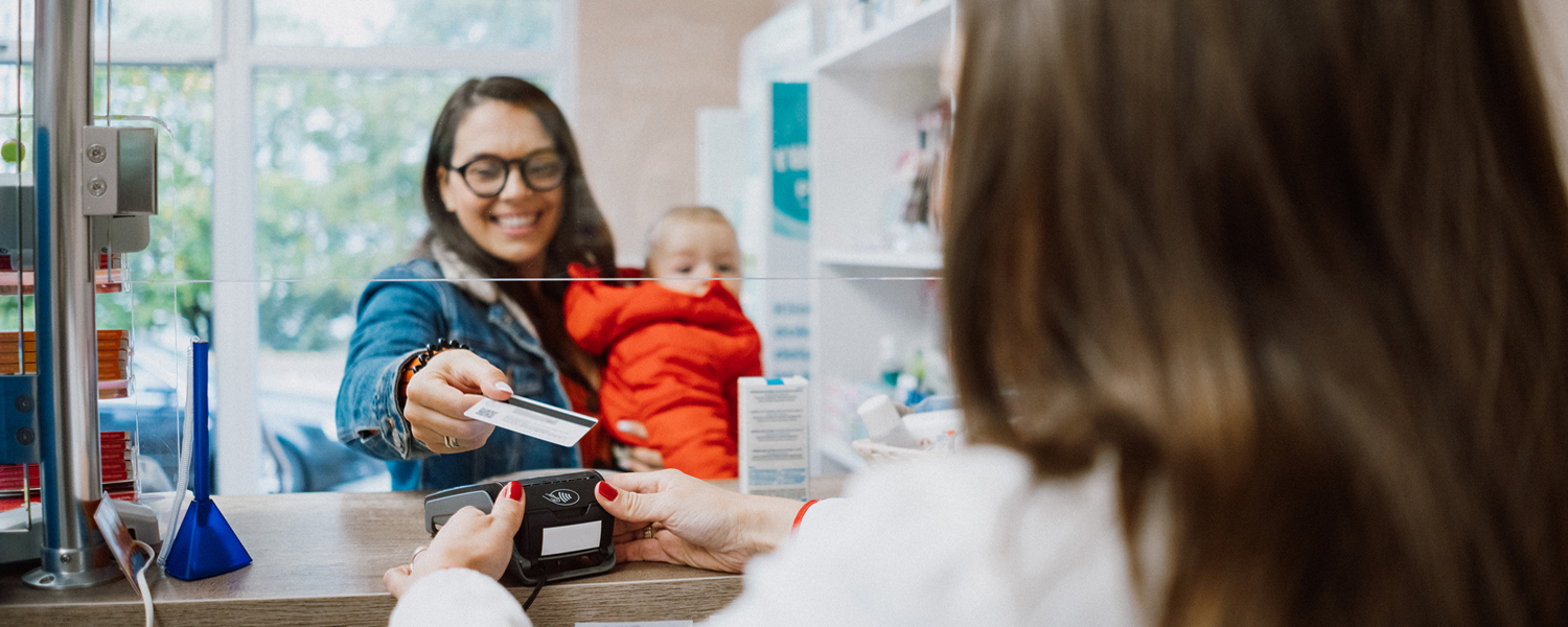 A woman holding a small child offers her credit card at a pharmacy counter