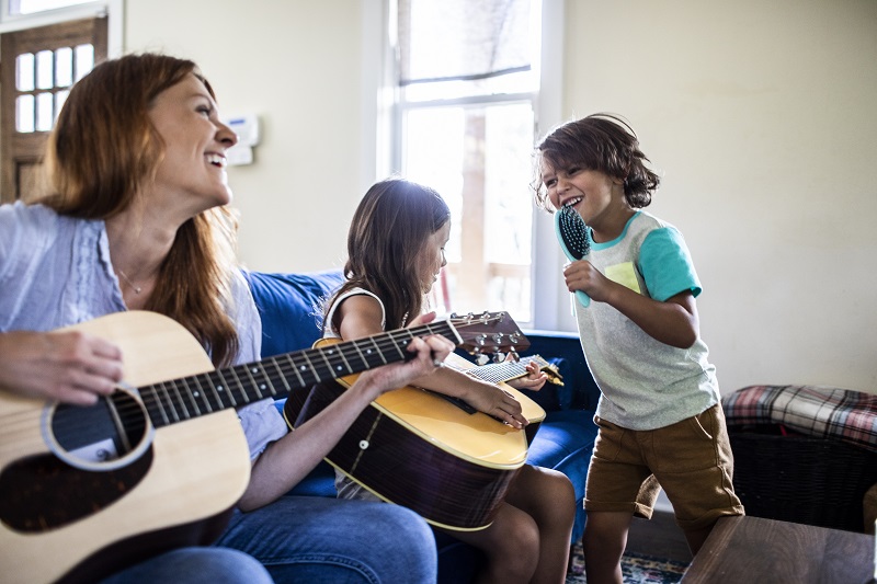 Mother and daughter playing guitar while son sings into a hairbrush