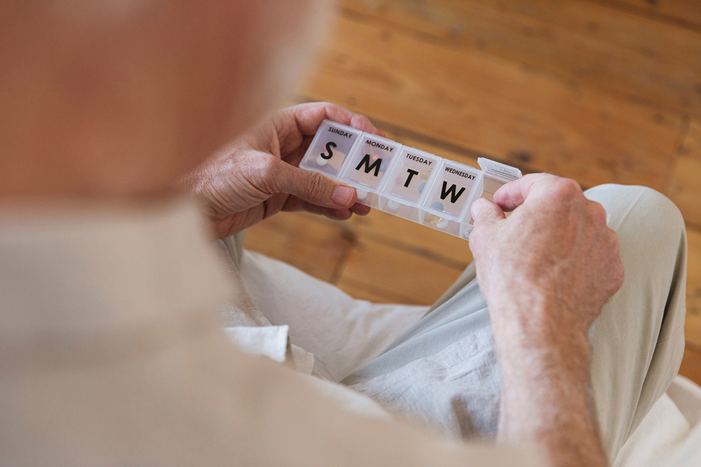 An older gentleman organizing prescriptions in a pill container. 