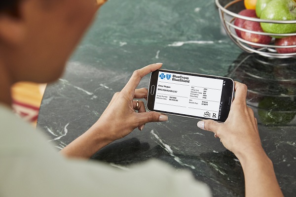 A woman holding a Blue Cross Blue Shield insurance card while on her laptop.