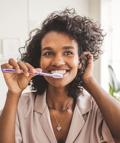 Mujer sonriendo mientras se cepilla los dientes.