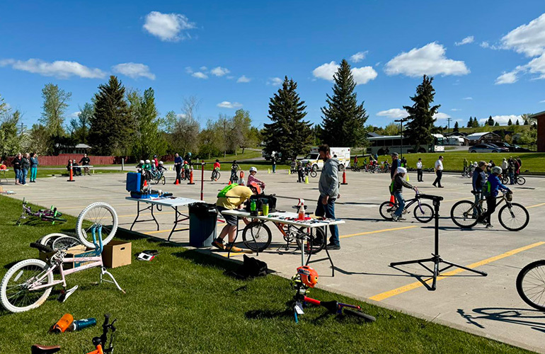 young kids ride bikes on concrete parking lot on sunny day with blue sky