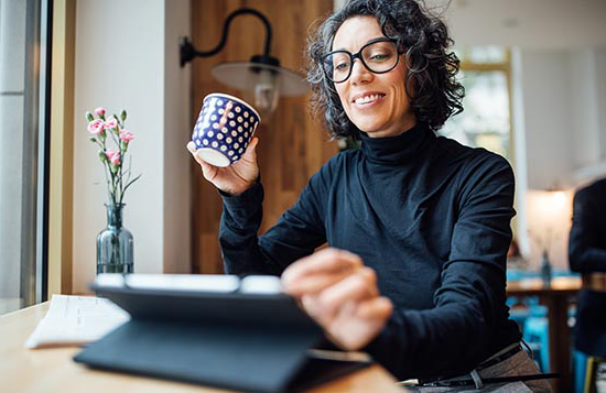 Female business professional using tablet computer and drinking coffee at coffee shop.