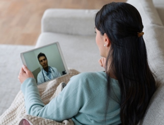 Woman seated on her couch talking with her doctor online via a tablet.