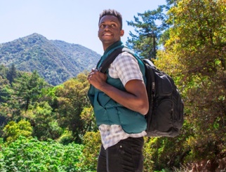 Young African American man wearing hiking clothes and a backpack with a mountain and trees in the background