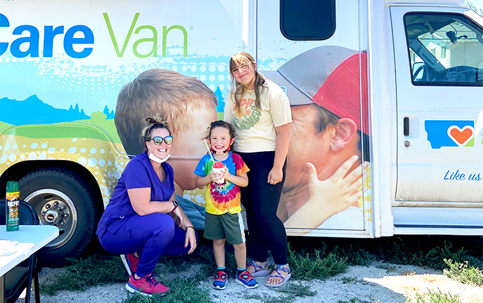 Young child and woman stand with Care Van that offers health services. 