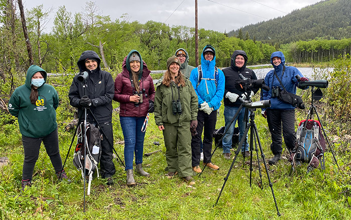 Eight young adults stand in marsh on native lands with surveying equipment.