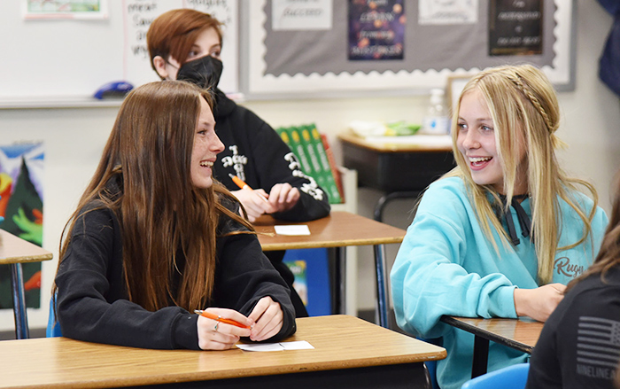 Girls sit at desks laughing during school.