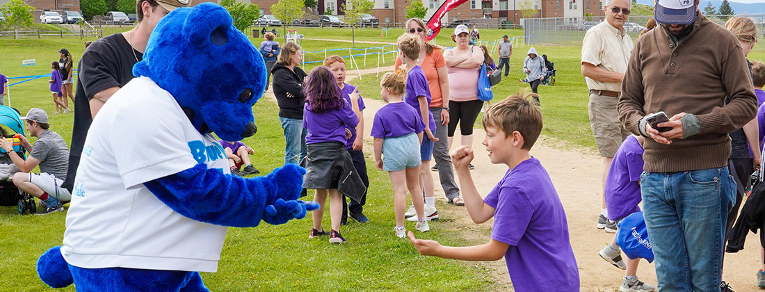 Blue Bear and child play game near families outside of school.