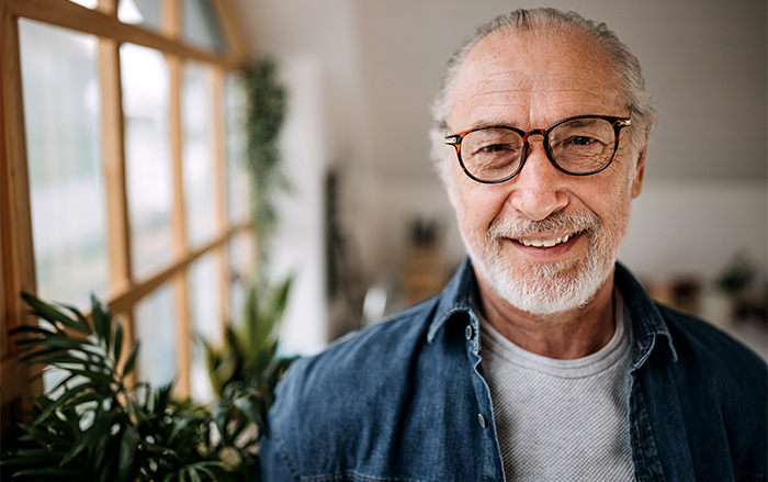 Man in glasses smiles near plants bordering a window.