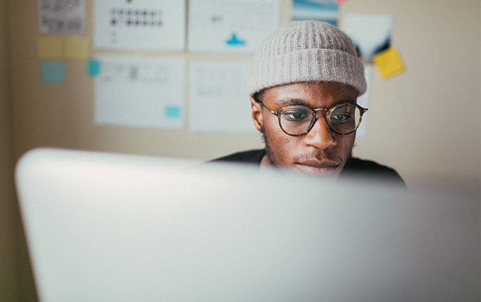 Black man wearing beanie looks at computer intently.