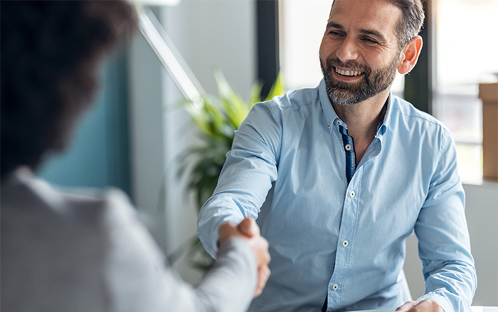 Bearded man in blue work shirt smiles while shaking hands.