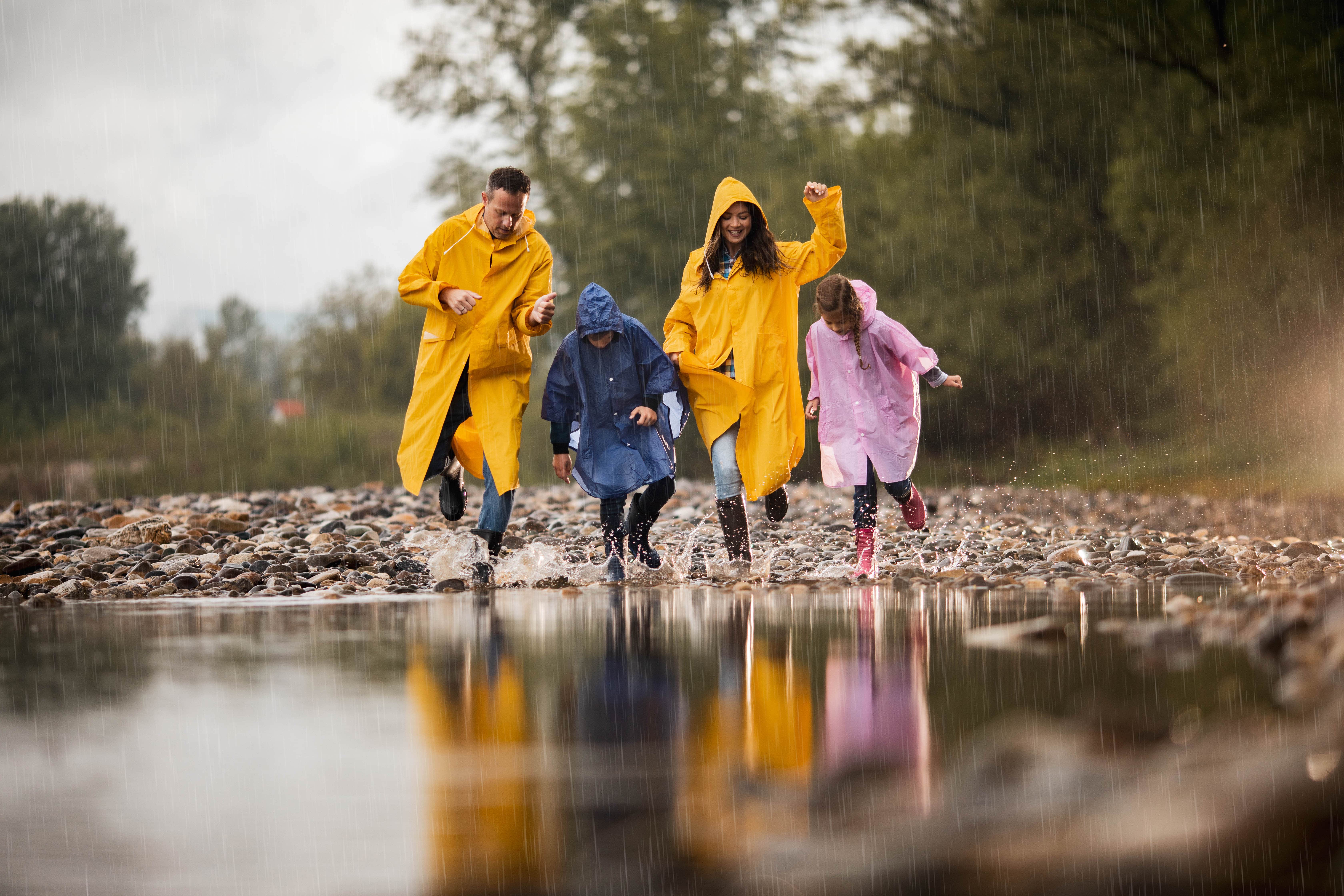 Family in rain boots and rain jackets dancing next to a large puddle
