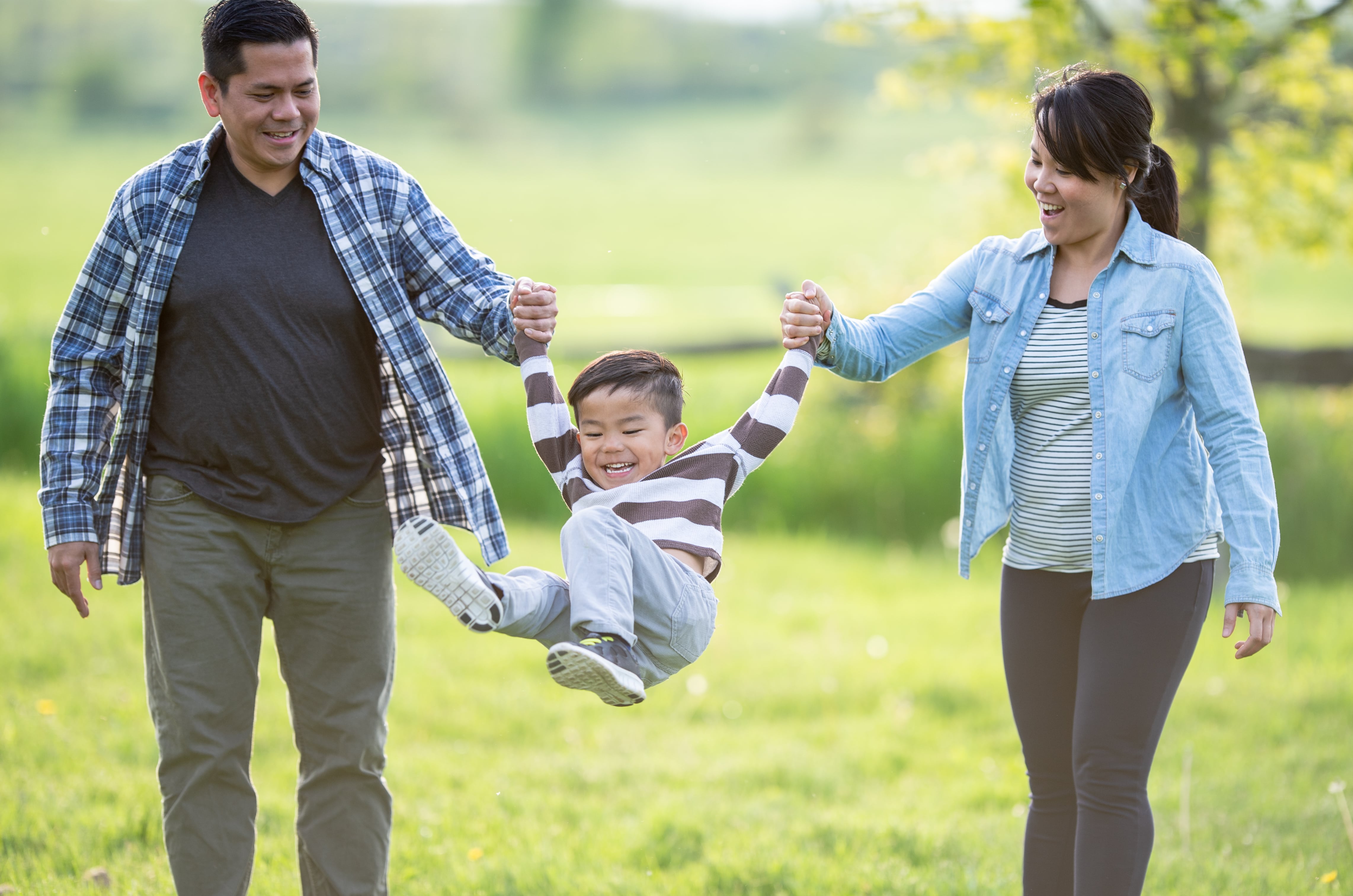 Man and woman in a field holding the hands of their smiling son and swinging him